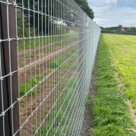 A close up image of a wire fence running along a grassy field.