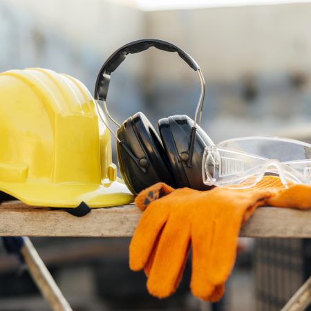 A wooden bench containing several PPE items, including a yellow hard hat, ear defenders, safety gloves and safety goggles/